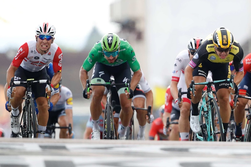 Caleb Ewan, left, grimaces as he pushes down on the pedals next to Peter Sagan in green and Dylan Groenewegen on right.