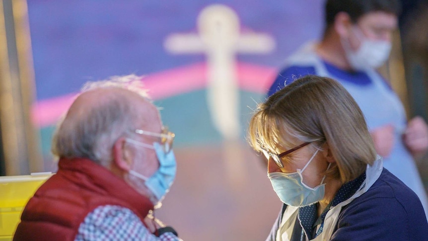 An elderly man is given a vaccination by a woman with dark glasses and a face mask