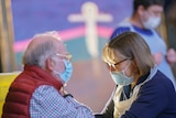 An elderly man is given a vaccination by a woman with dark glasses and a face mask