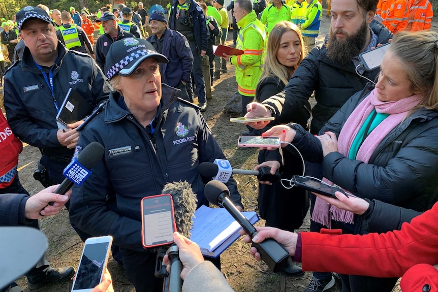 Journalists holding their phones out in front of a police officer at a press conference.