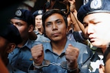 Tight shot of a man in handcuffs surrounded by guards.