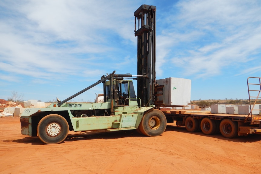 A forklift lifts large stone blocks onto a truck. 