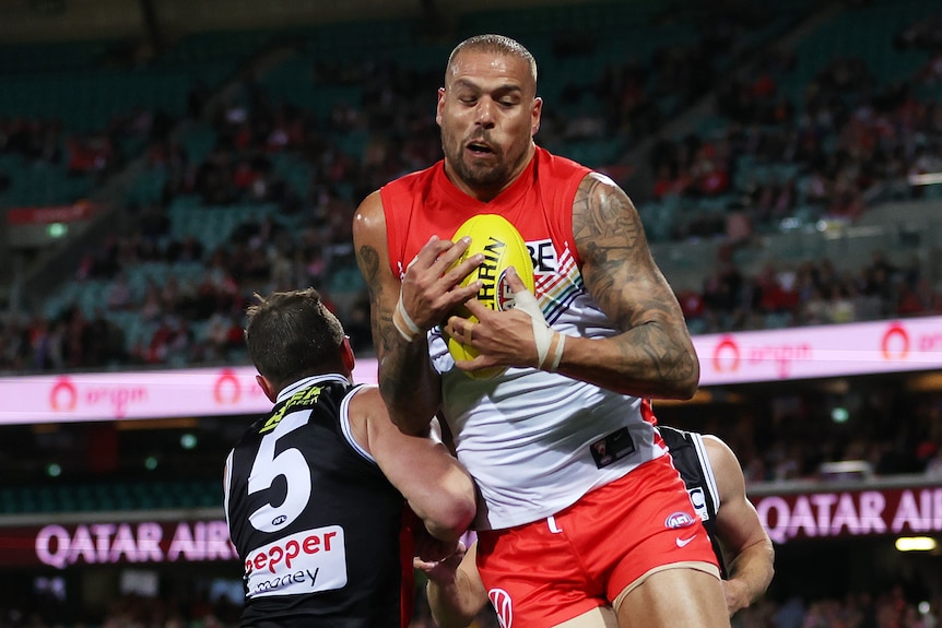 Lance Franklin holds the ball and grimaces as an opponent bumps into him