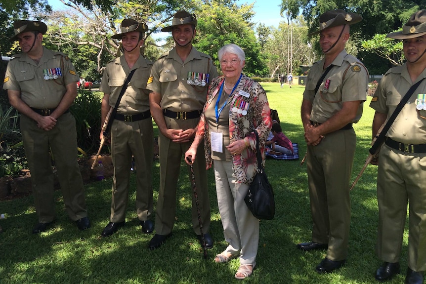 Veteran Anne Dawson smiles and poses with current military personnel with greenery in the background.