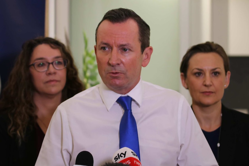 A mid-shot of WA Premier Mark McGowan speaking at a media conference in front of two women.