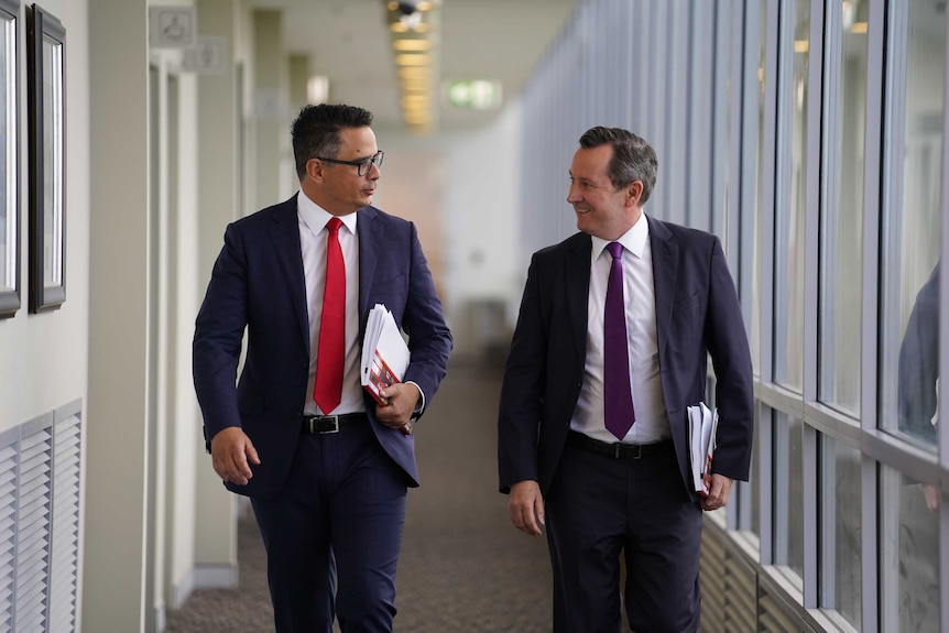 Mr Wyatt and Mr McGowan look at each other while walking down a corridor. Mr Wyatt holds the WA Budget