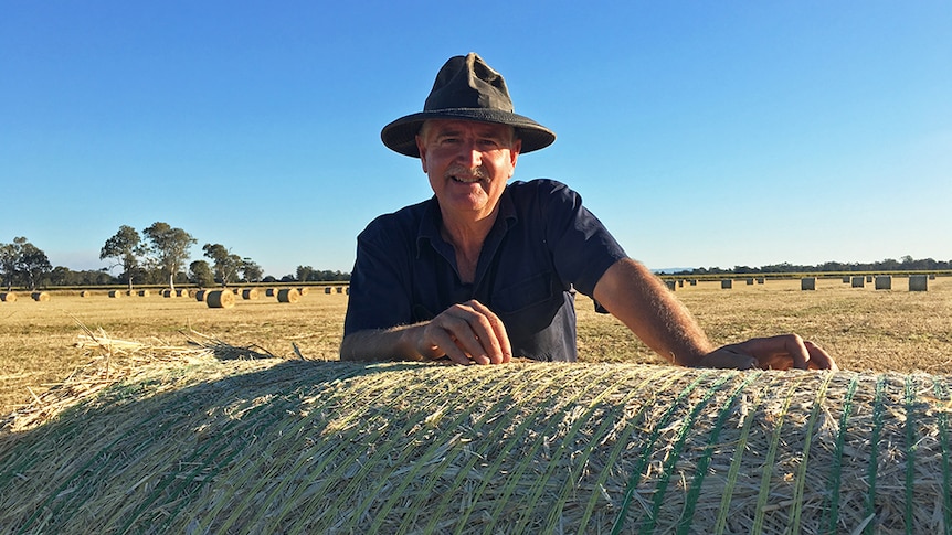 Kelvin Hamilton leans over a bale of hay.