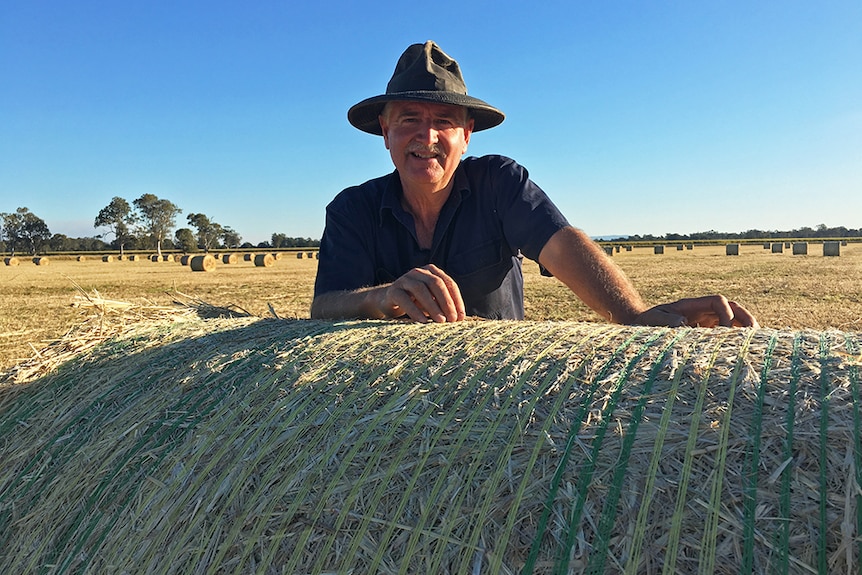 Kelvin Hamilton leans over a bale of hay.