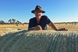 Kelvin Hamilton leans over a bale of hay.