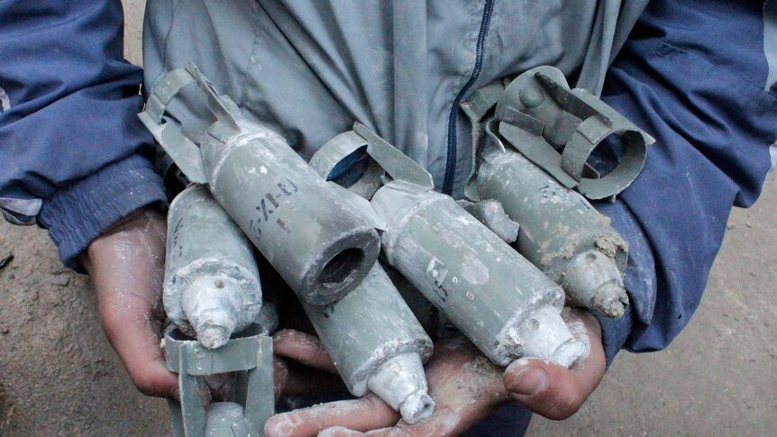 A boy holds several unexploded small canisters.