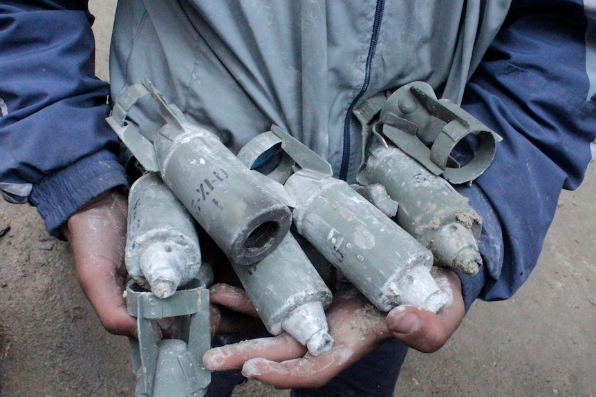 A boy holds several unexploded small canisters.