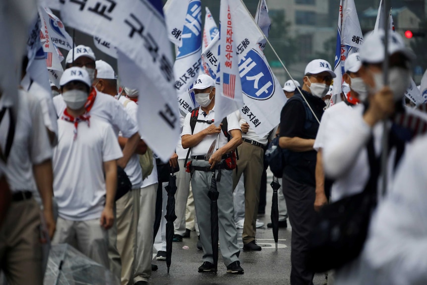 A group of people wearing masks stand holding signs on a street.