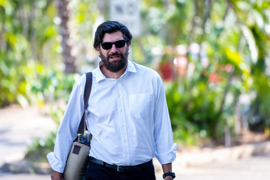 A bearded man with black hair carrying a laptop bag.