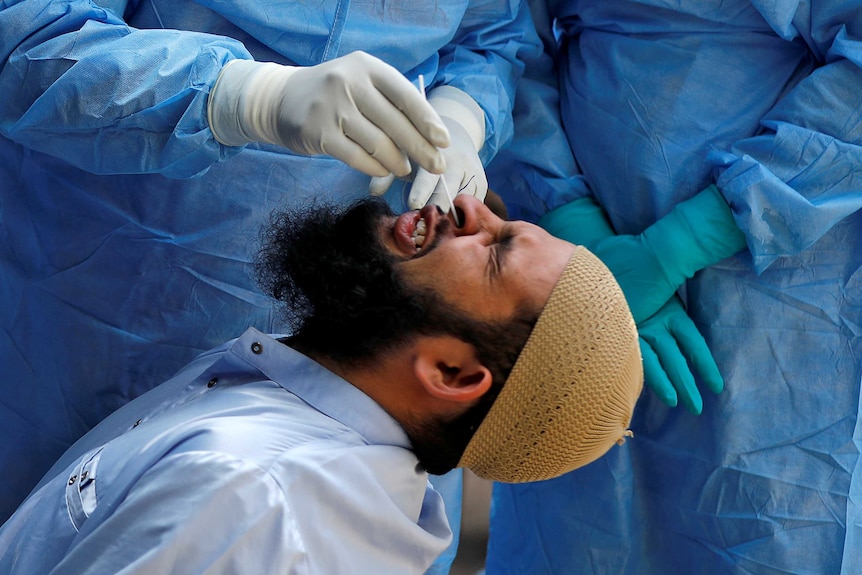 A man winces as people in personal protective gear stick a swab down his nose