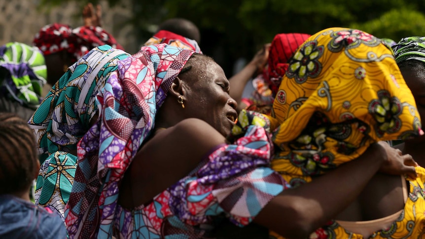 A woman cries and embraces one of the released Chibok school girls. They are dressed in bright traditional attire.