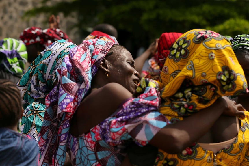 A woman cries and embraces one of the released Chibok school girls. They are dressed in bright traditional attire.