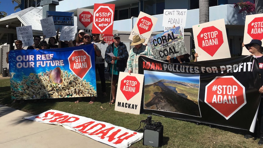 A group of about 20 protesters stand with signs that read "stop Adani".