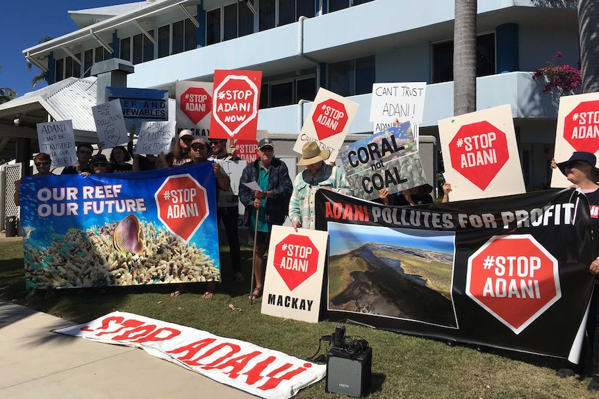 A group of about 20 protesters stand with signs that read "stop Adani".