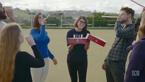 Woman holds birthday cake while others surround her and blow party whistles