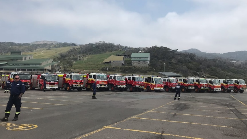 Several fire trucks in a car park, with a steep mountain rising behind it.