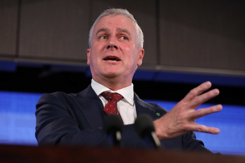 A low angle shot of McCormack giving a speech, gesturing with his right hand.