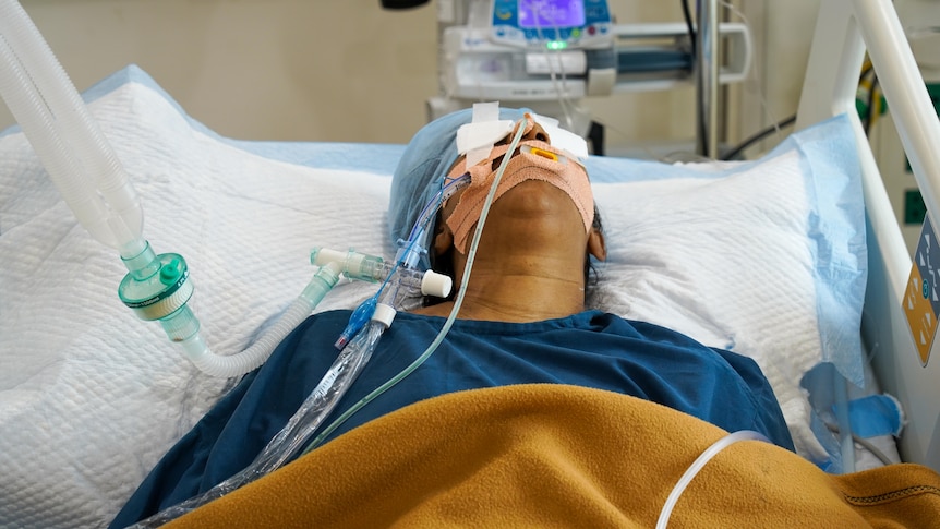 A woman in a hospital bed attached to a ventilator