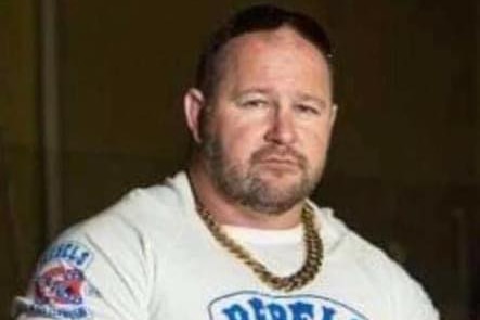 Mr Martin wears a white tshirt with 'Rebels' on it and two crossed guns. He also wears a very thick gold chain and has arm tatts