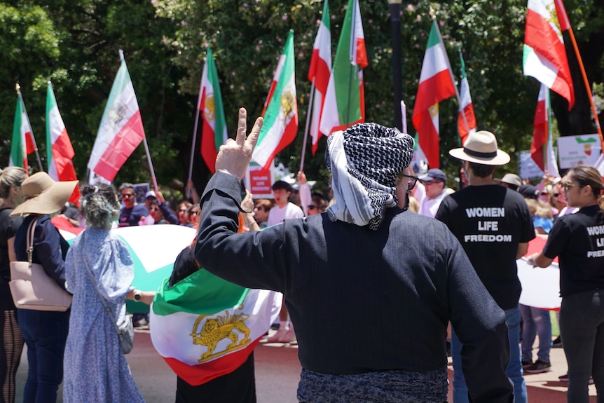 A ma dressed in black holds up a peace sign with his back to the camera. 