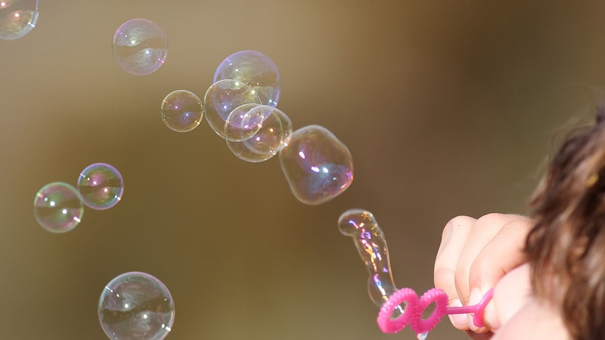 A child blowing bubbles using a pink bubble blower.