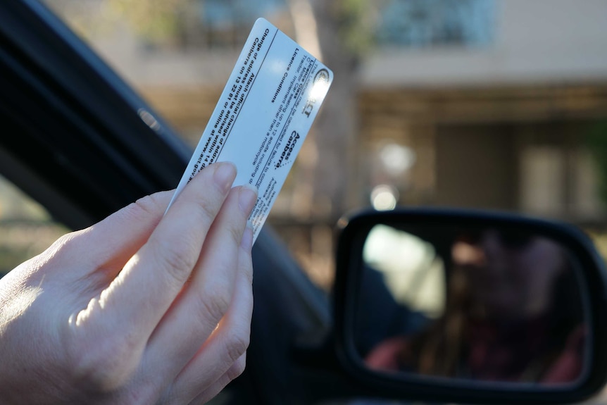 A hand holds an ACT driver's license out a car window.