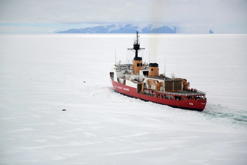 A red and white ship cutting through a body of icy water.
