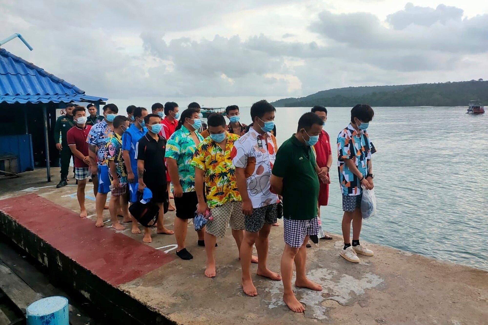 A group of Chinese men wearing brightly coloured holiday clothing and masks stand on a pier.