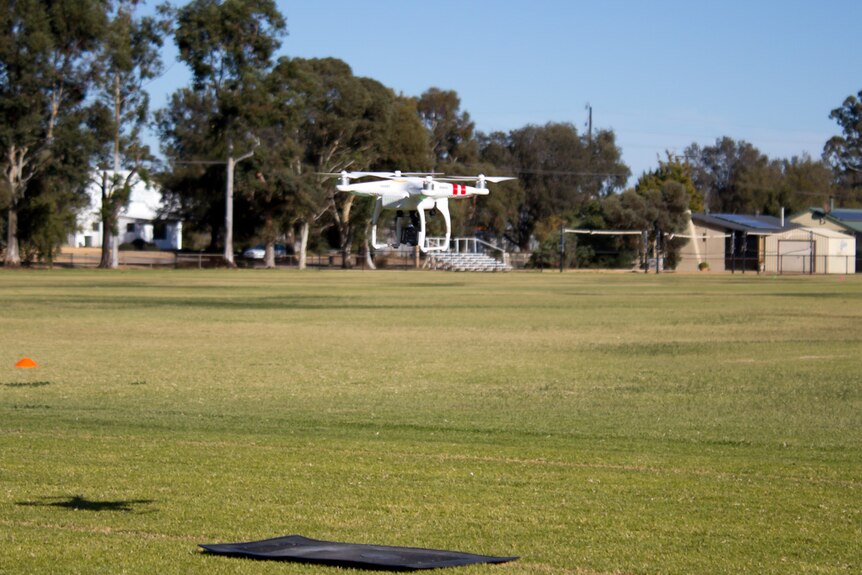 A drone hovering above a landing mat on a school oval.