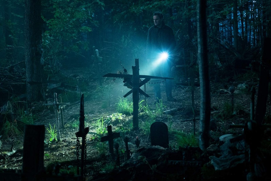 In a dark forest, the actor shines his torch to illuminate a makeshift/DIY graveyard.