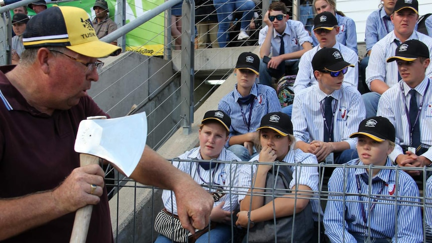 A group of students watch as a man holds an axe.