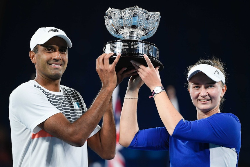 Mixed doubles partners stand on either side of the trophy, holding it aloft at the Australian Open.