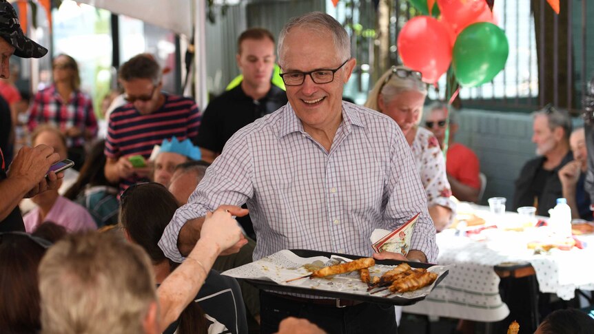 Malcolm Turnbull holds a tray of food and shakes hands with an attendee at Christmas Day lunch