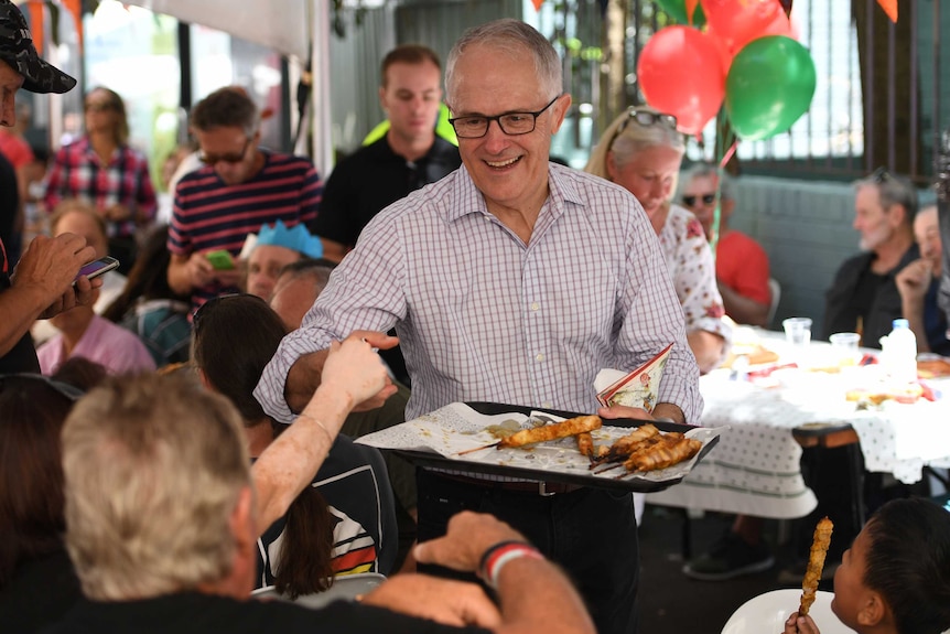 Malcolm Turnbull holds a tray of food and shakes hands with an attendee at Christmas Day lunch