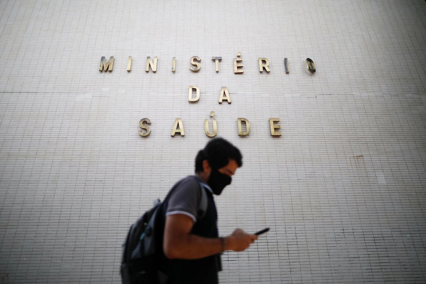 a man walks in front of a building sign while on his phone