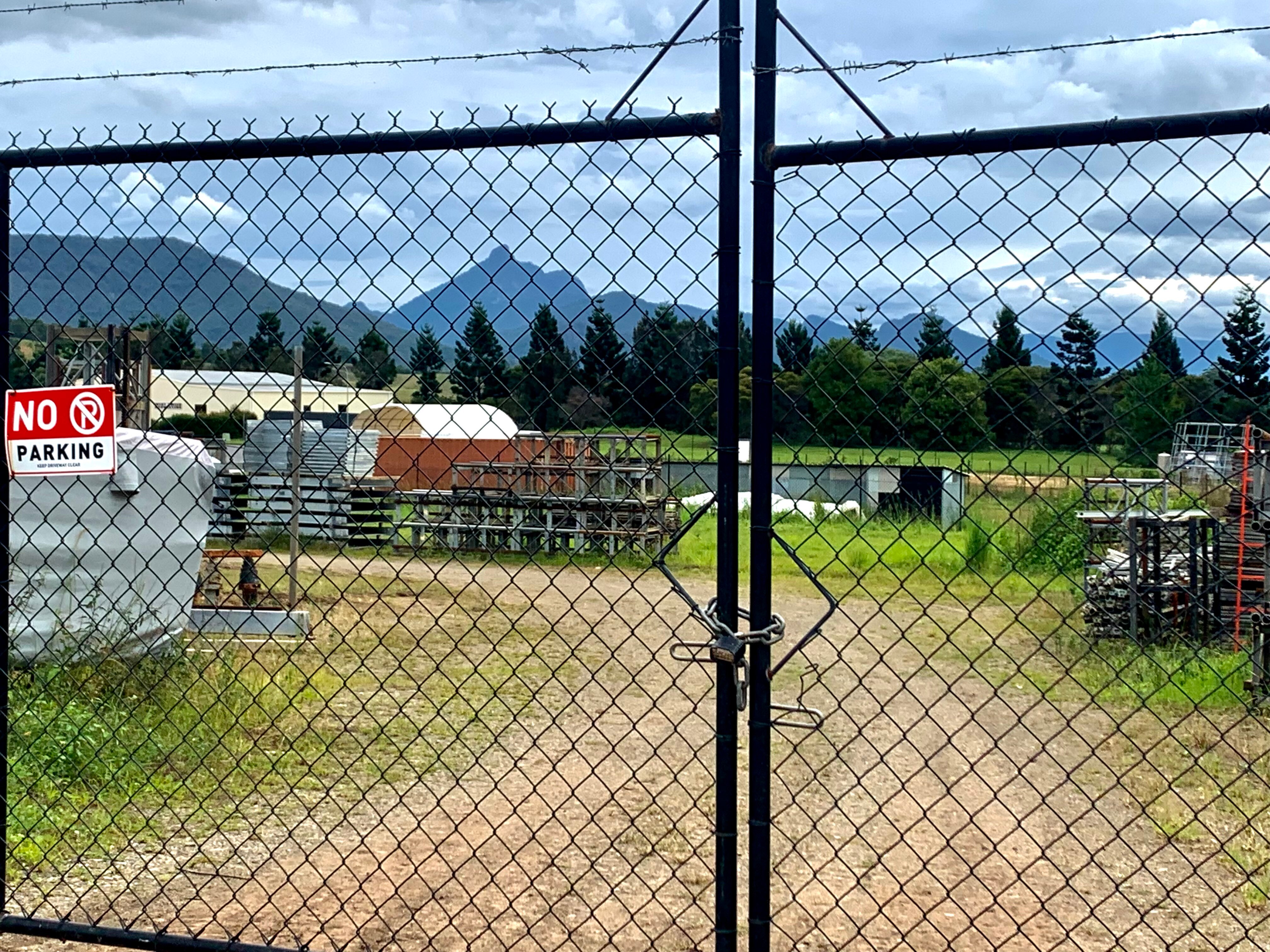 Locked black security fence in foreground with view of industrial estate and Wollumbin/Mt Warning in the background 