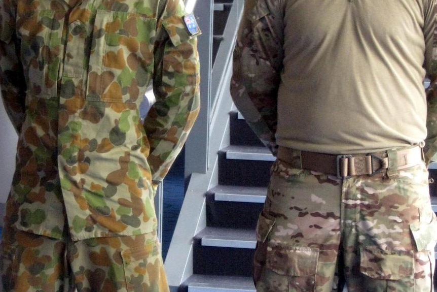 Two soldiers in combat attire stand side by side. Their faces are not visible.