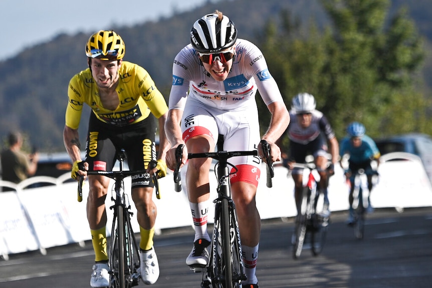 Two cyclists, one in a white jersey ahead of one in yellow, straining as they ride.