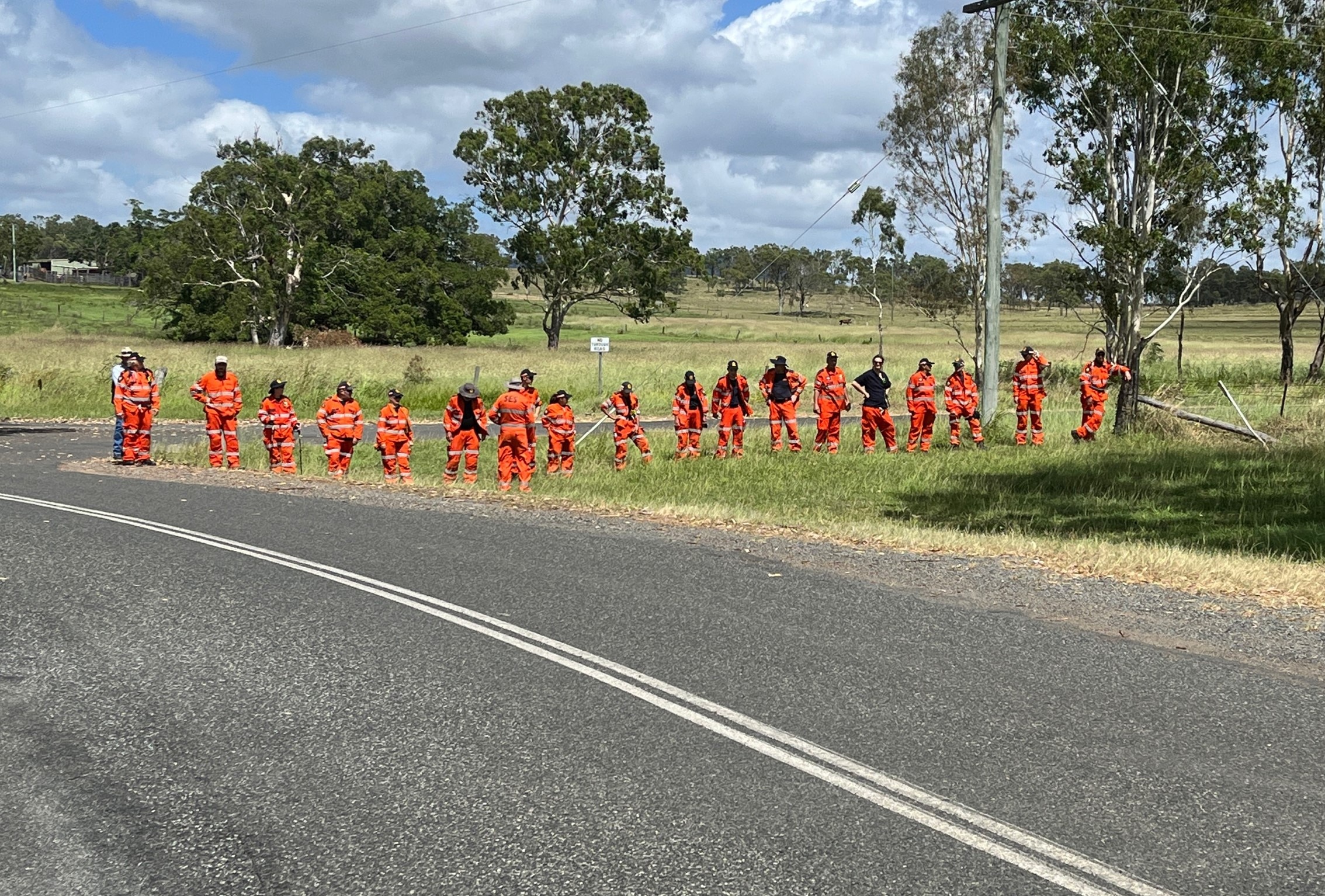 A line of people in orange uniforms standing on grass, waiting. 