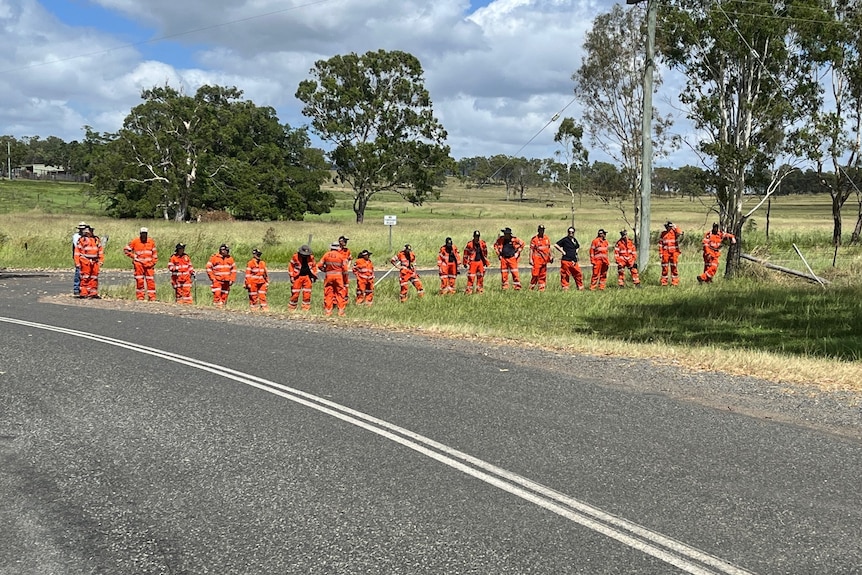 A line of people in orange uniforms standing on grass, waiting. 
