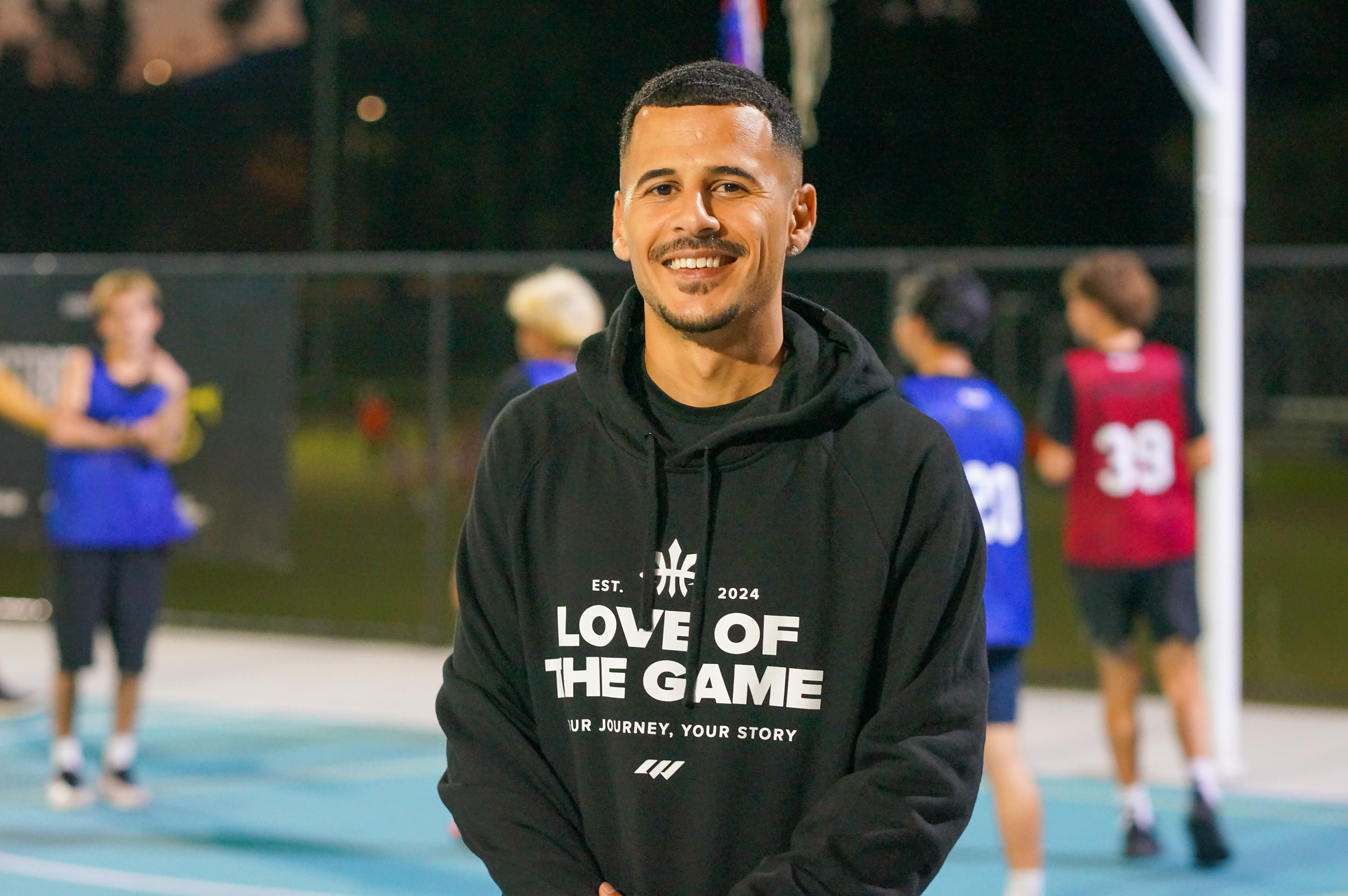 Saleh Jaidi wearing a black hoodie stood in front of kids playing basketball