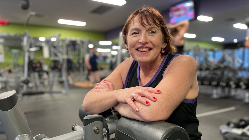 Raelene Roede is sitting on exercise equipment inside a gym and smiling at the camera