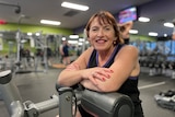 Raelene Roede is sitting on exercise equipment inside a gym and smiling at the camera