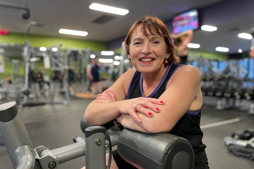 Raelene Roede is sitting on exercise equipment inside a gym and smiling at the camera