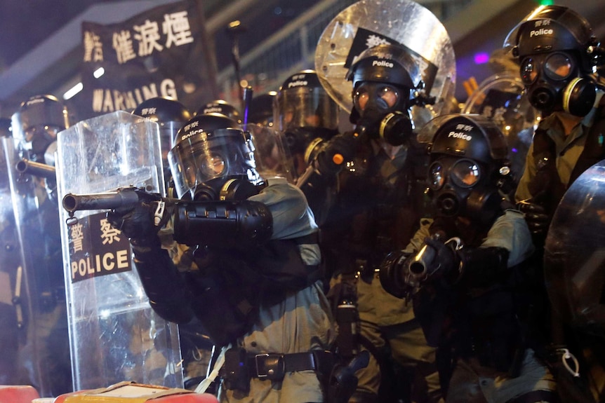 Police in riot gear holding plastic shields and pointing guns