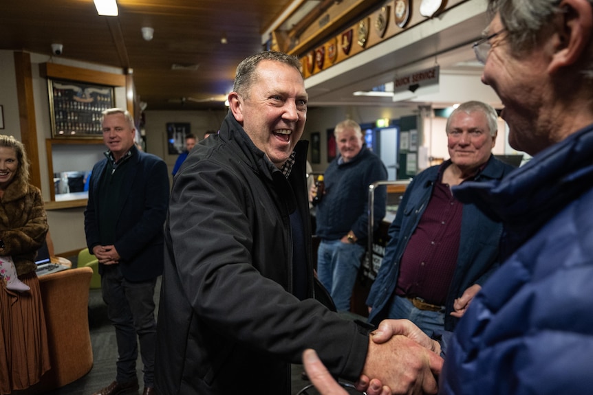 A man shakes hands with another man at a bar.